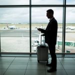 Businessman with luggage using mobile phone at airport